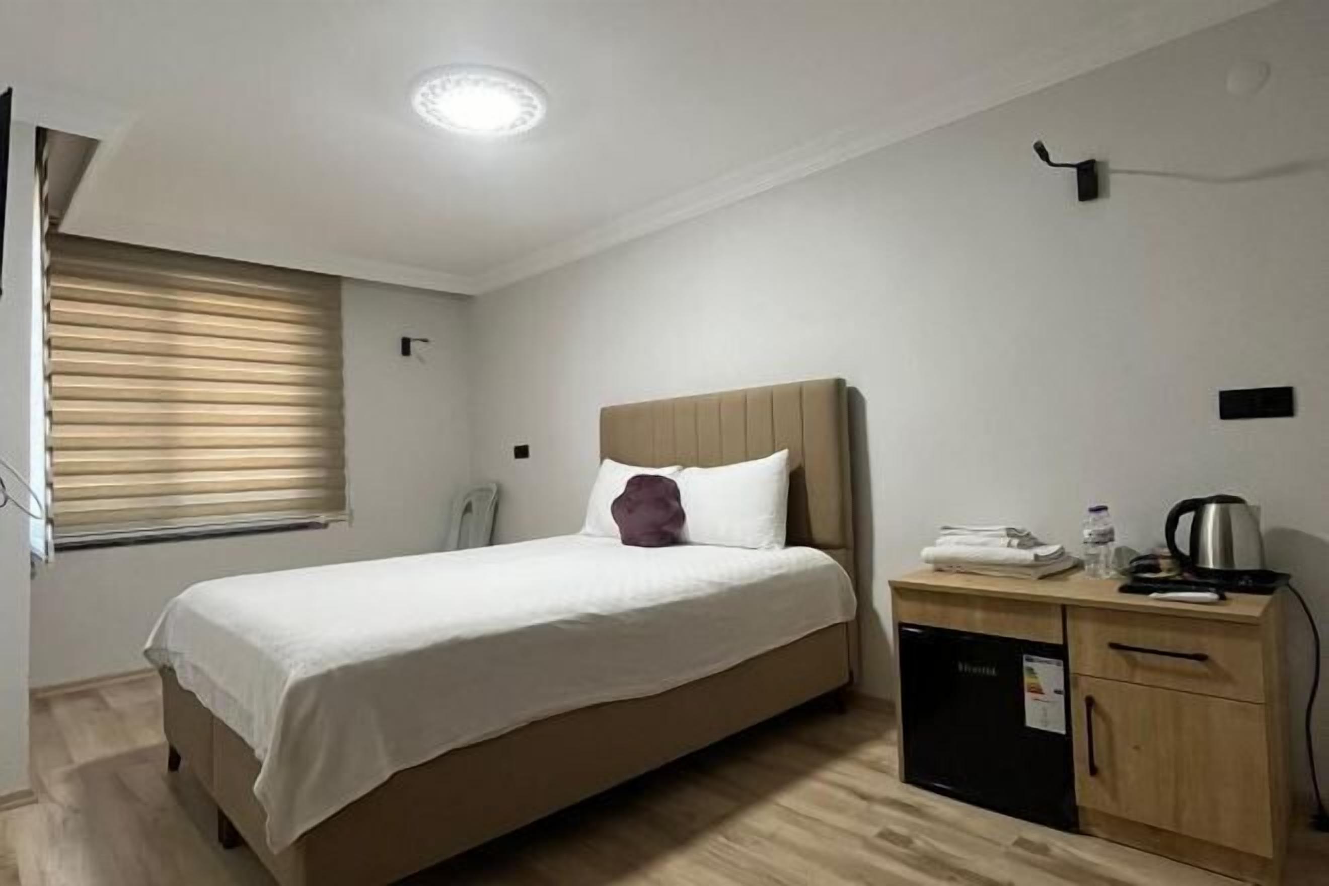 Un dormitorio con cama, mesita de noche, un mueble pequeño y una ventana con persianas.