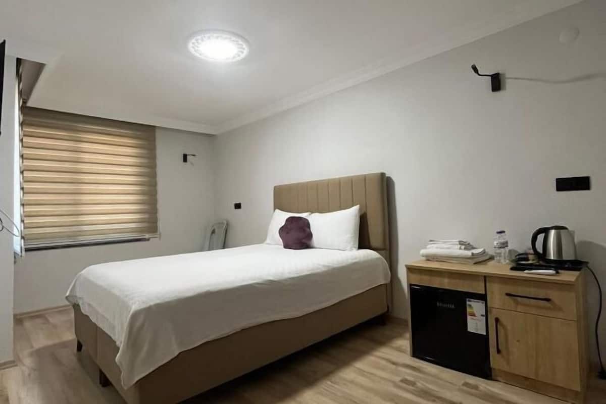Une chambre à coucher comprenant un lit, une table de chevet, une petite armoire et une fenêtre avec des stores.