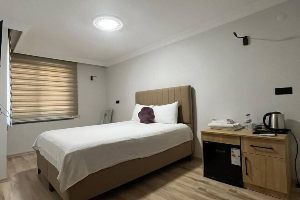 Une chambre à coucher comprenant un lit, une table de chevet, une petite armoire et une fenêtre avec des stores.