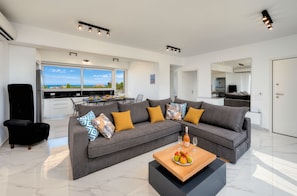 A modern living room with a grey sectional sofa, a black armchair, and a wooden coffee table with fruit. - Luminosa Luxury Villa Private Pool (Apokoronas)