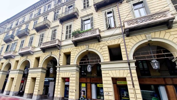 Un immeuble à plusieurs étages, doté de fenêtres en arc de cercle et de balcons, et dont la façade comprend un commerce avec une enseigne indiquant « Poste ».