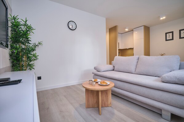 Un salon moderne avec un canapé gris, une table basse ronde en bois et une plante en pot.