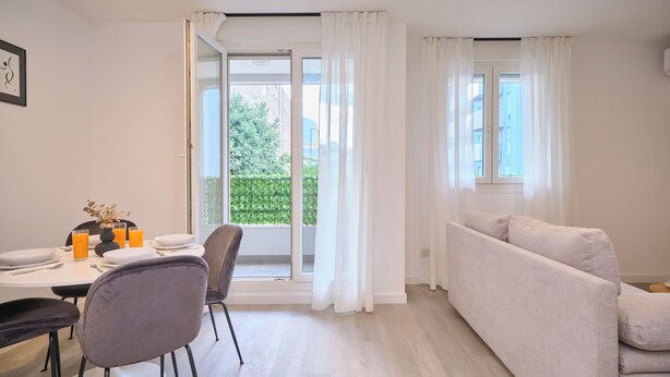 A modern living room with a sofa, dining table, chairs, and a sliding glass door leading to a balcony. - Point of Life 1 by Litto (Split)