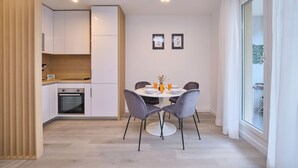 A modern kitchen with white cabinets, a built-in oven, and a dining area with a round table and two chairs. - Point of Life 1 by Litto (Split)