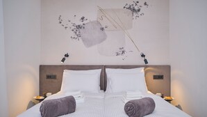 A neatly made bed with white linens and two folded towels, a wall-mounted light fixture, and a small table with a plate and a cup. - Point of Life 1 by Litto (Split)