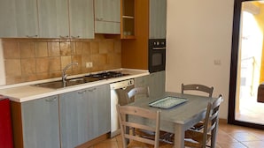 Een keuken met grijze kastjes, een fornuis en een eettafel met stoelen.