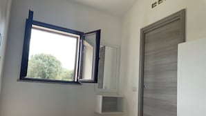 Een slaapkamer met een bed, een raam, een spiegel en een deur.