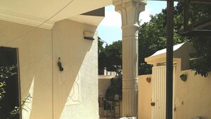 Un espace extérieur abrité, doté d’une balustrade en pierre, d’une porte blanche et d’un petit jardin avec une chaise et un pot de fleurs.