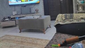 Un salon comprenant un téléviseur, un canapé, un pouf et un tapis à motifs.