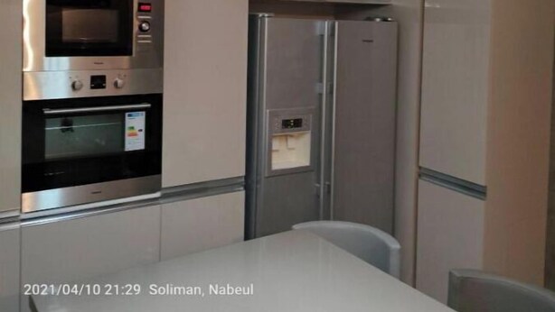 Une cuisine moderne dotée d’appareils électroménagers en acier inoxydable, notamment un four à micro-ondes, un four et un réfrigérateur. Des luminaires suspendus sont placés au-dessus du plan de travail.