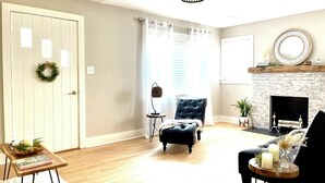 A living room with a fireplace, a black armchair, a wooden coffee table, and a white door with a wreath. - “Delightful Decor” & “SO CLOSE” to Beech Bend, WKU, Caves, & Corvette Museum! (Bowling Green)