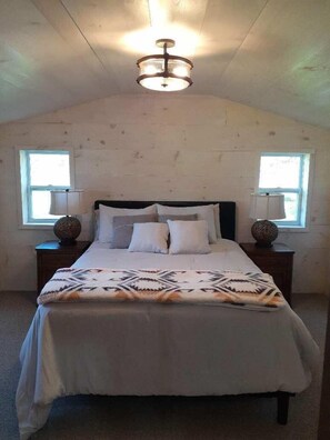 A bedroom with a bed, two nightstands, a ceiling light fixture, and two windows.