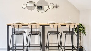 A modern dining area with a wooden table set for four, black bar stools, and a decorative wall piece above the table. - Ettrick Court House By REDWOOD STAYS (Farnborough)