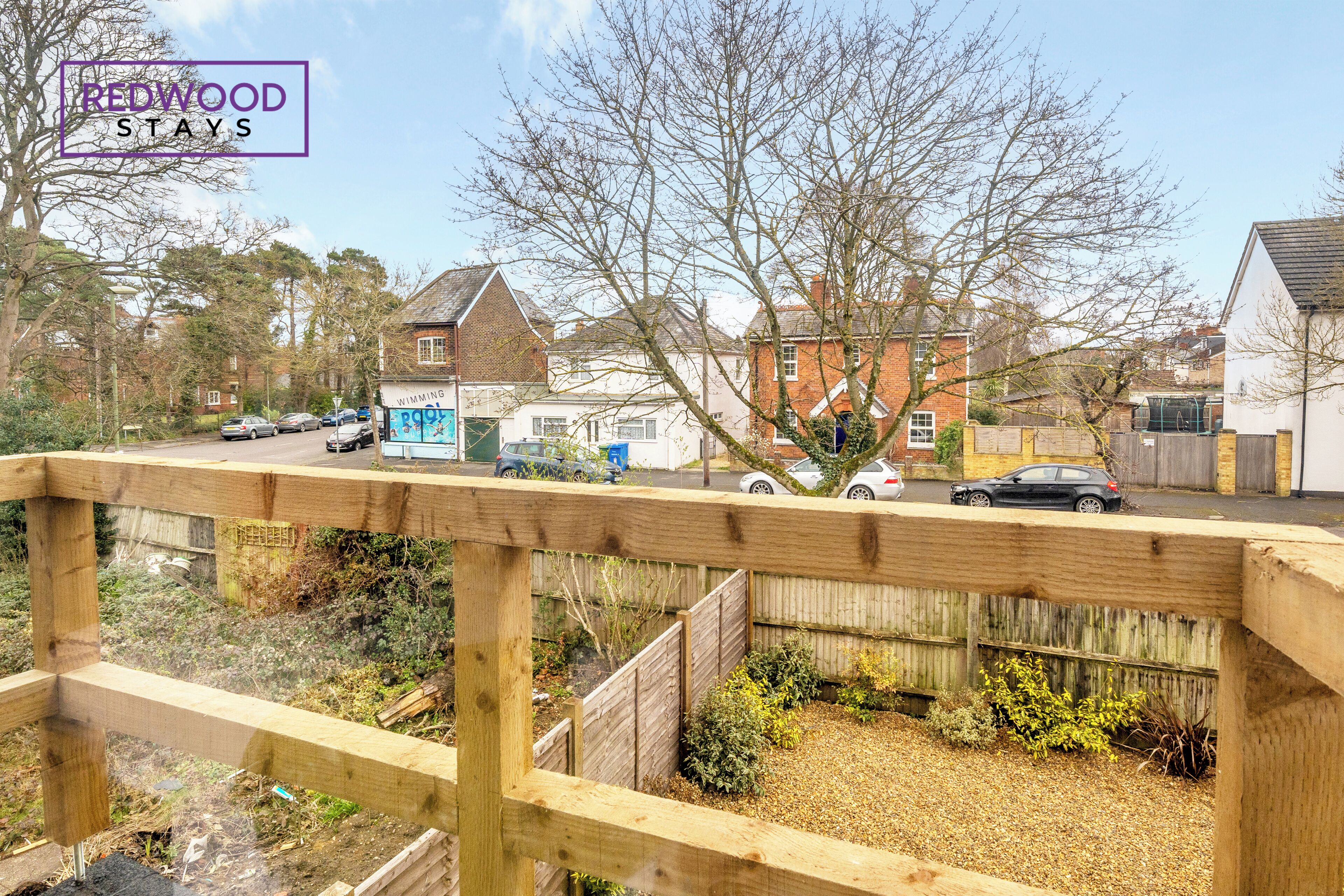 A residential area with a wooden fence, a garden, and houses in the background.