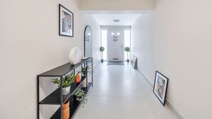 A hallway with a black console table displaying potted plants and framed artwork, leading to a door with a sign. - Ettrick Court House By REDWOOD STAYS (Farnborough)