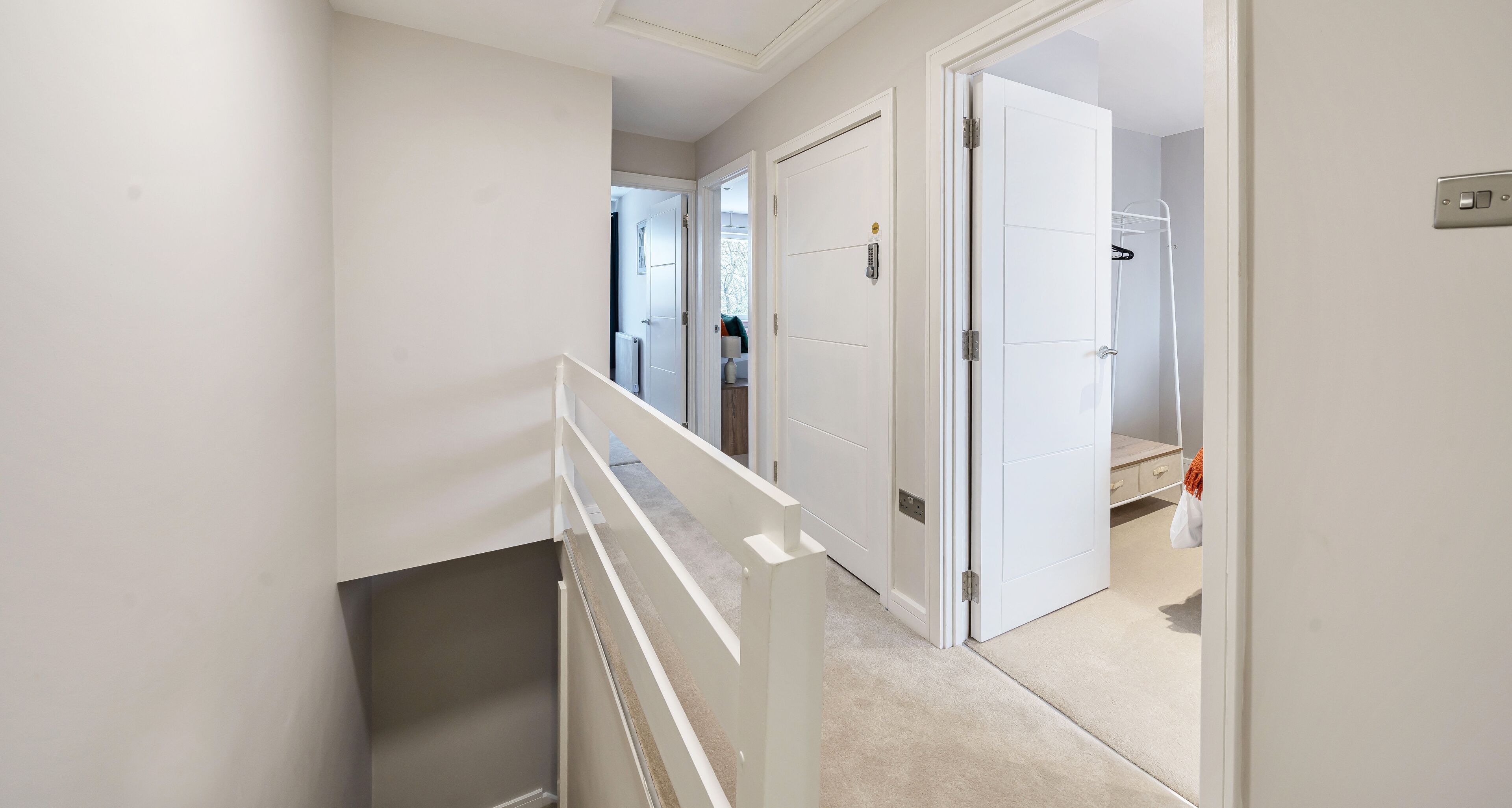 Een gang met witte wanden, een tapijtvloer en een witte leuning. Er zijn deuren die leiden naar andere kamers.