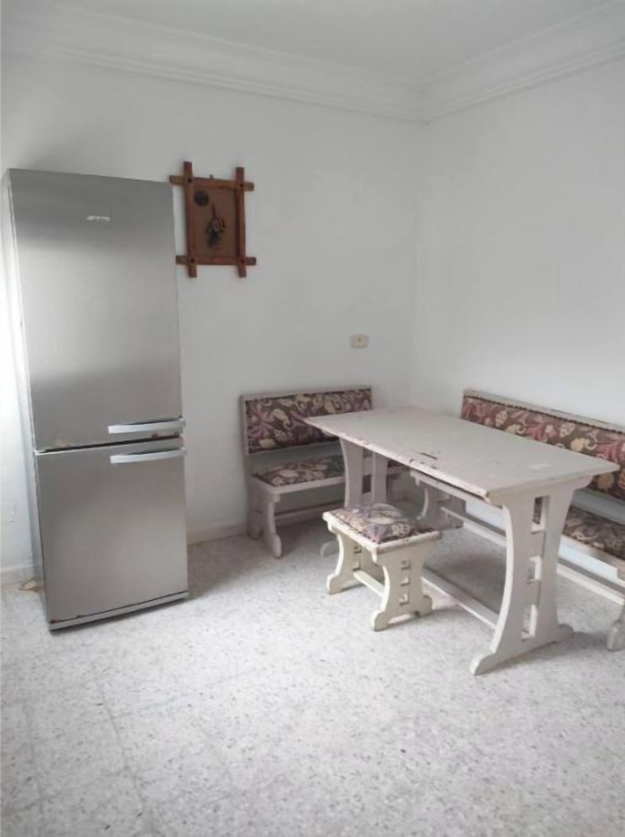 Una cocina compacta con refrigerador, banco y mesa.