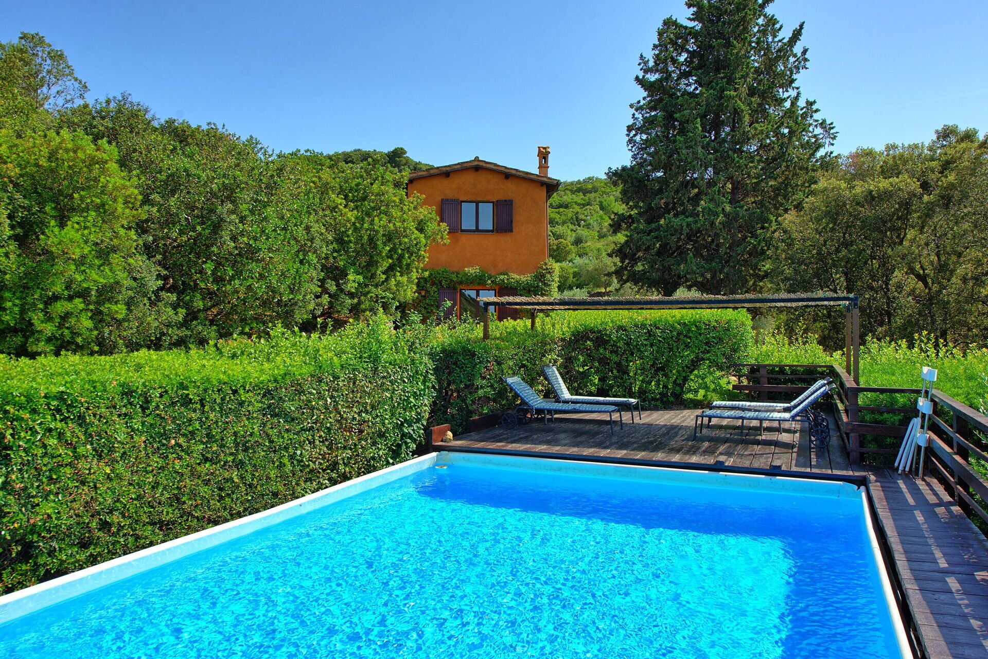 Ein Schwimmbecken mit Liegestühlen, einer Holzterrasse und einem Haus im Hintergrund.