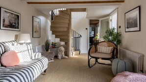 A cozy living room with a striped sofa, a rocking chair, a staircase, and framed pictures on the walls. - Stunning cottage with modern twists and original features - Carpenters Cottage (Sandford St Martin)