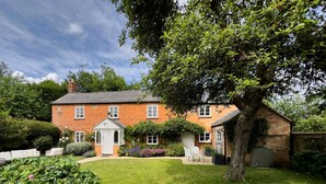 A brick house with a white door, a small garden, and a tree in front. - Stunning cottage with modern twists and original features - Carpenters Cottage (Sandford St Martin)