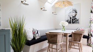 A dining area with a round table, wicker chairs, a bench with cushions, a potted plant, and wall-mounted lights. - Stunning cottage with modern twists and original features - Carpenters Cottage (Sandford St Martin)