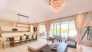 Ein modernes Wohnzimmer mit Essbereich, einem großen Fenster mit Vorhängen, einer Chandelieber und einer Lampe.