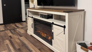 Un salon moderne avec un téléviseur à écran plat fixé sur un meuble blanc, une cheminée en dessous et un plancher en bois.