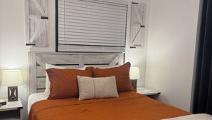 Une chambre avec un grand lit, deux tables de chevet, un ventilateur de plafond et une fenêtre avec des stores.