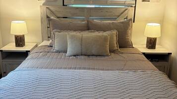 Un dormitorio con cama, dos lámparas de noche, una ventana con persianas y cabecera con diseño rústico.