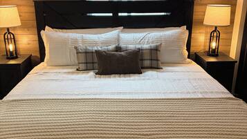 A neatly made bed with white linens and a brown throw blanket, flanked by two bedside lamps with exposed bulbs.