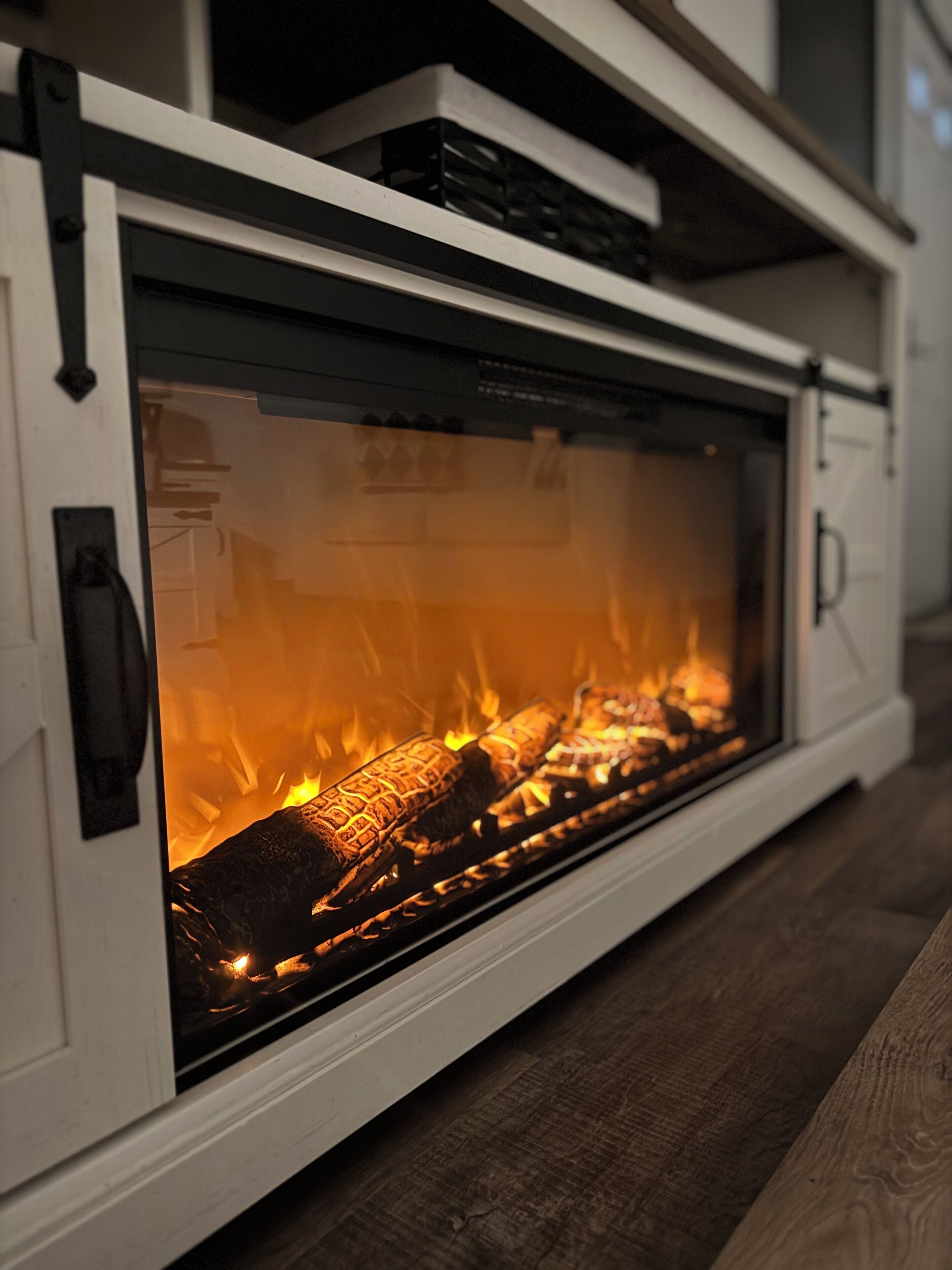 A fireplace with a glass front, logs burning inside, and a white mantelpiece.