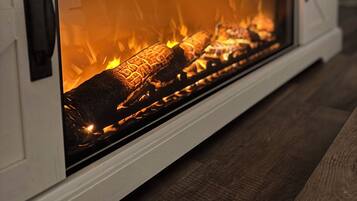 A fireplace with a glass front, logs burning inside, and a white mantelpiece.