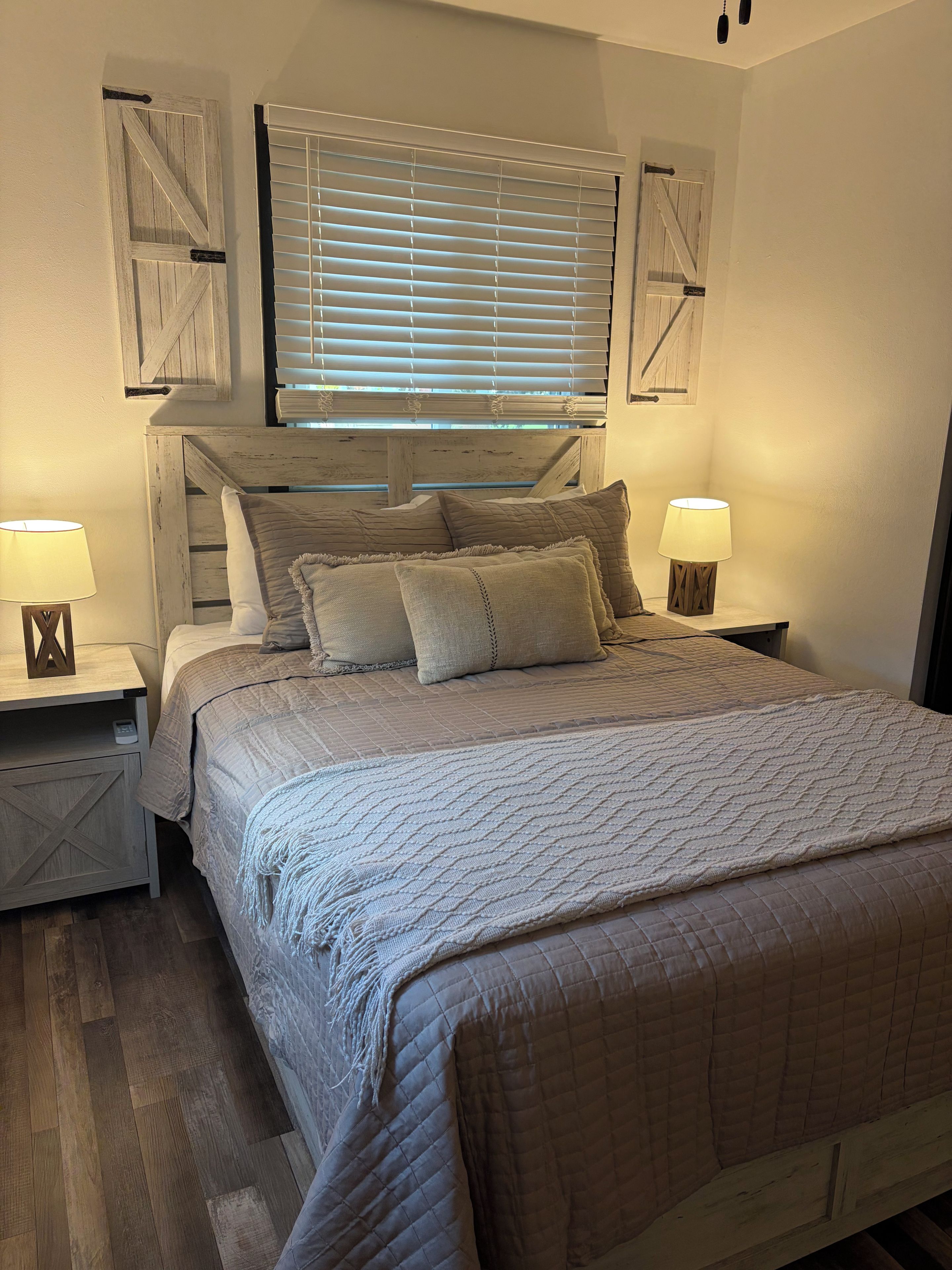 Un dormitorio con cama, dos mesitas de noche, una lámpara de pared y una ventana con persianas.