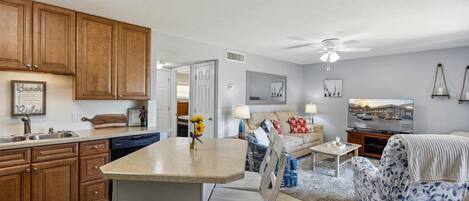 A kitchen with wooden cabinets, a dining area with a table and chairs, a sofa, and a television.