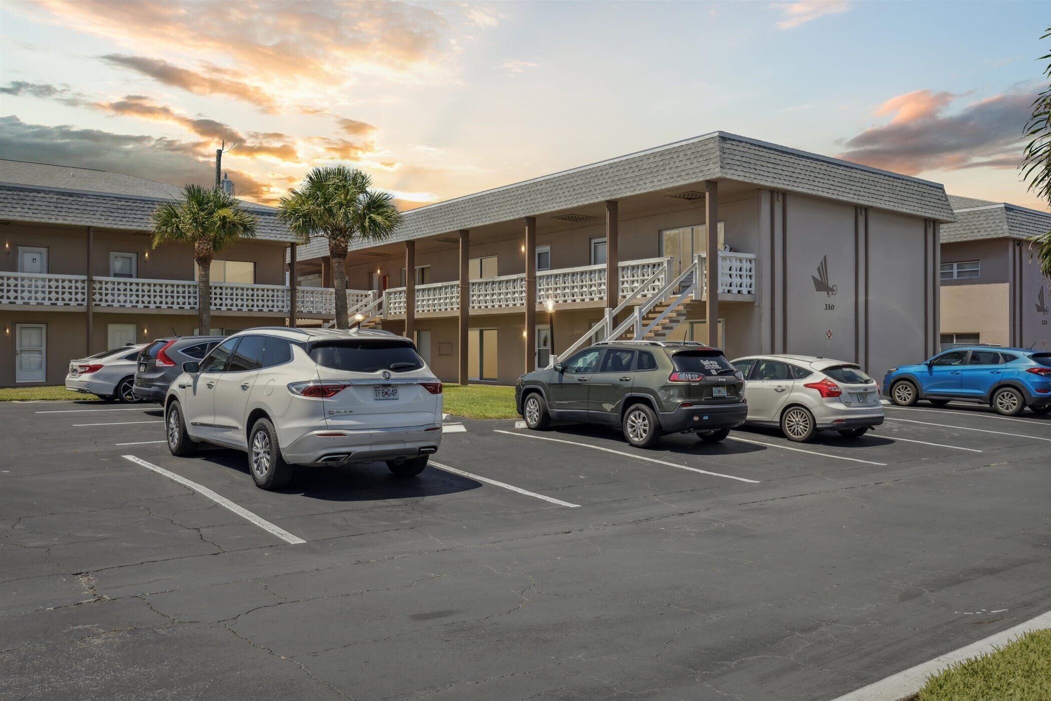 Hotel com estacionamento, vários carros e céu ao pôr do sol.