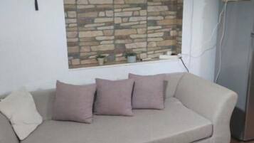 Un salon avec un canapé beige, un mur en pierre, une petite table et un tapis blanc.