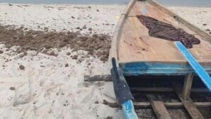 Un bote de madera sobre una playa arenosa, con un mar tranquilo al fondo.