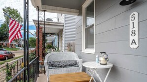 A porch with a wicker sofa, a wooden bench, a small table with a candle and a lantern, and a house number sign. - Historic Ludlow Suites (Covington)