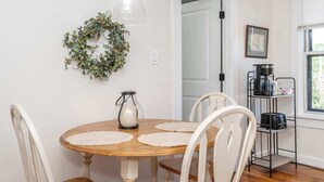A dining area with a wooden table, white chairs, a hanging light fixture, a wreath, and a coffee station. - Historic Ludlow Suites (Covington)
