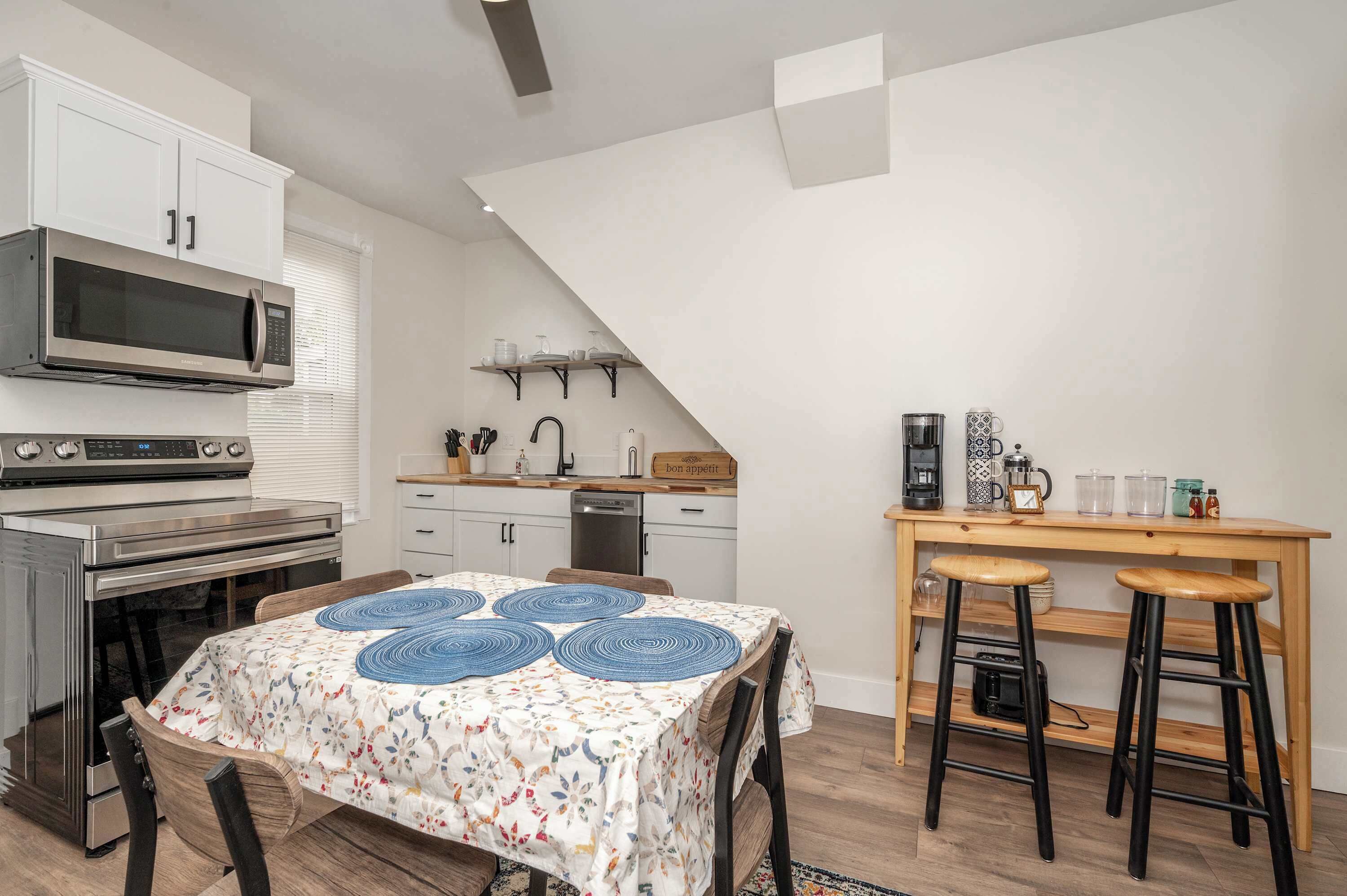 A compact kitchen with a microwave, stove, and wooden table with stools.