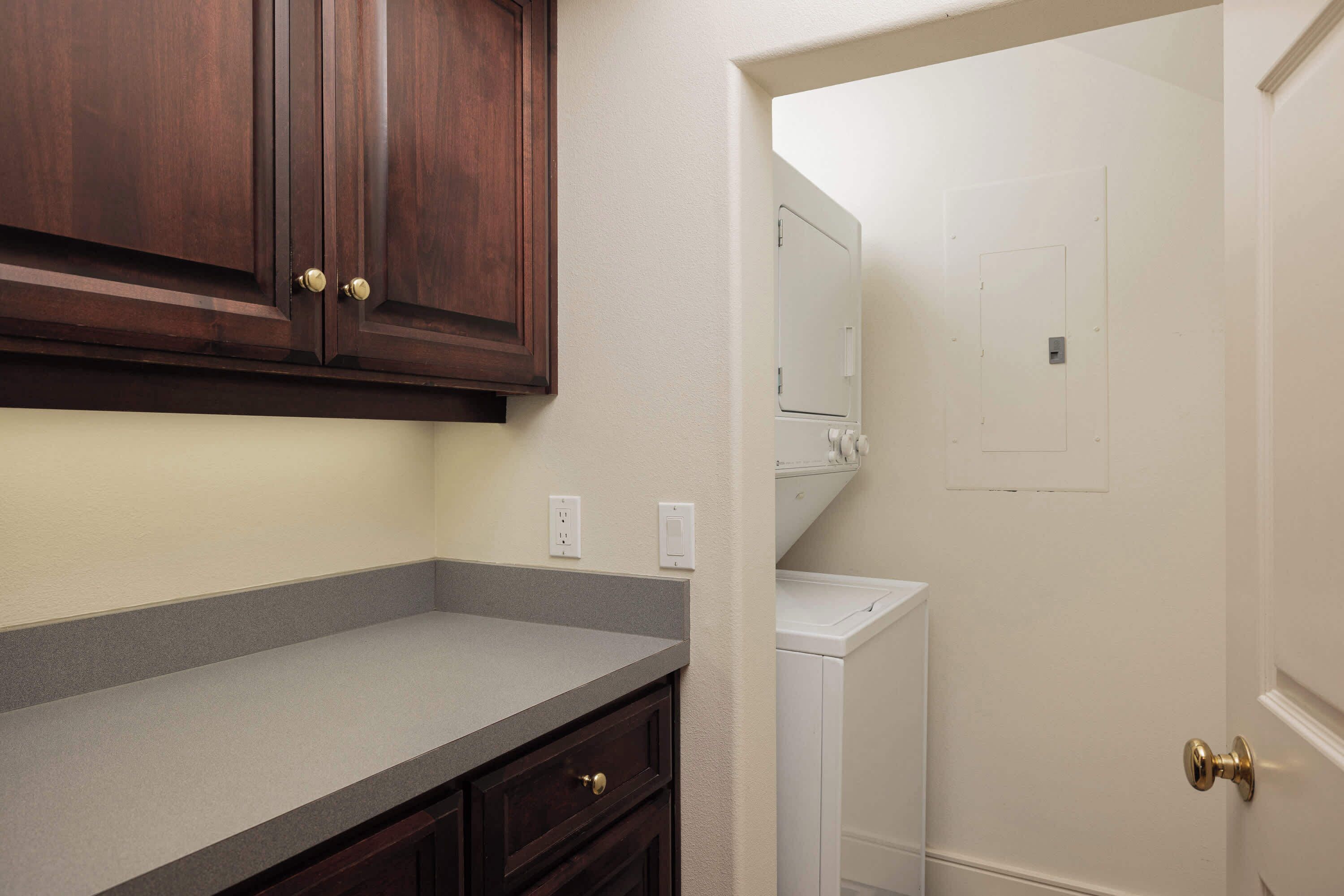 A kitchen with dark wooden cabinets, a grey countertop, and a white door leading to a laundry area.