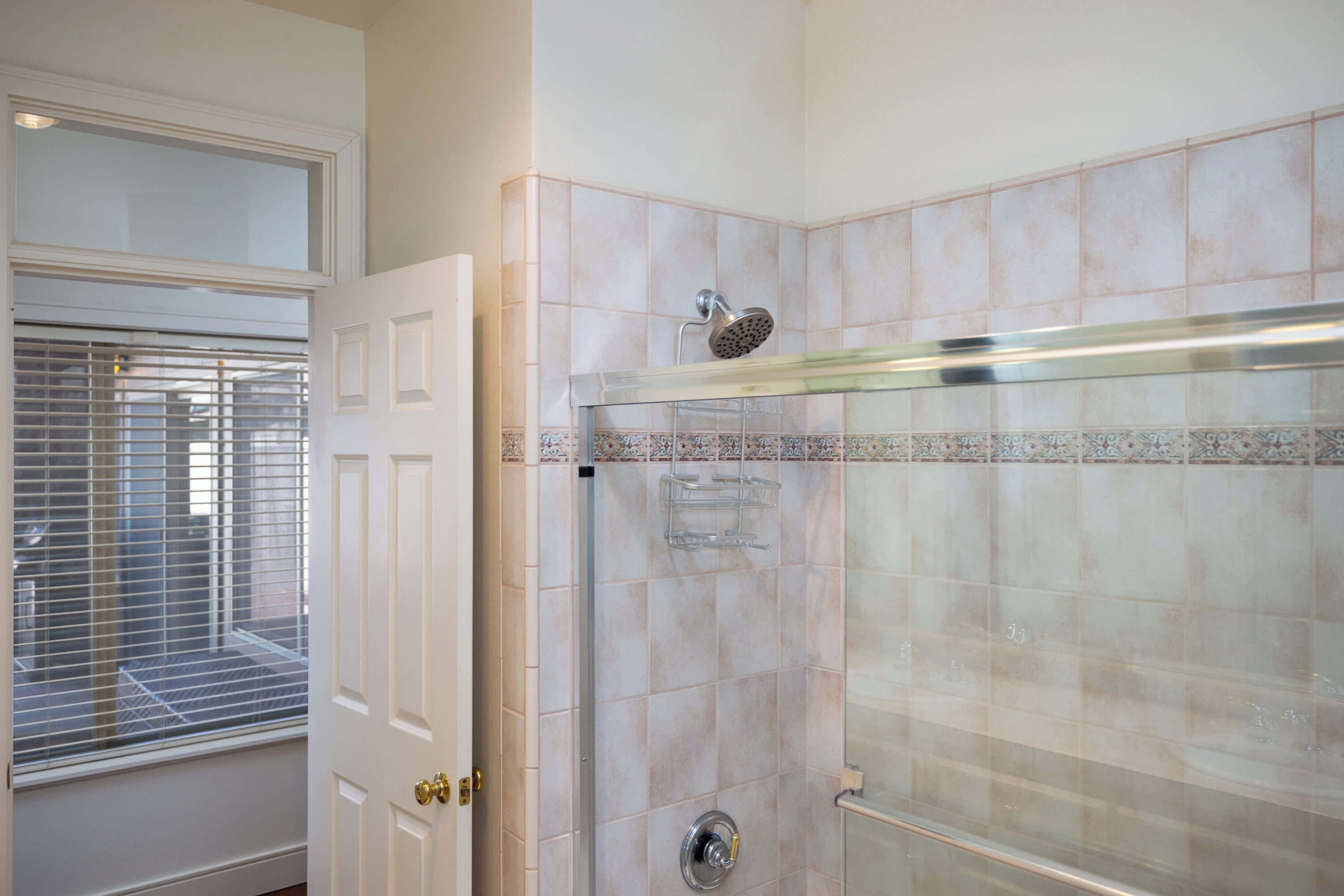 Une salle de bain avec une douche à parois de verre, des murs carrelés et une fenêtre avec des stores.