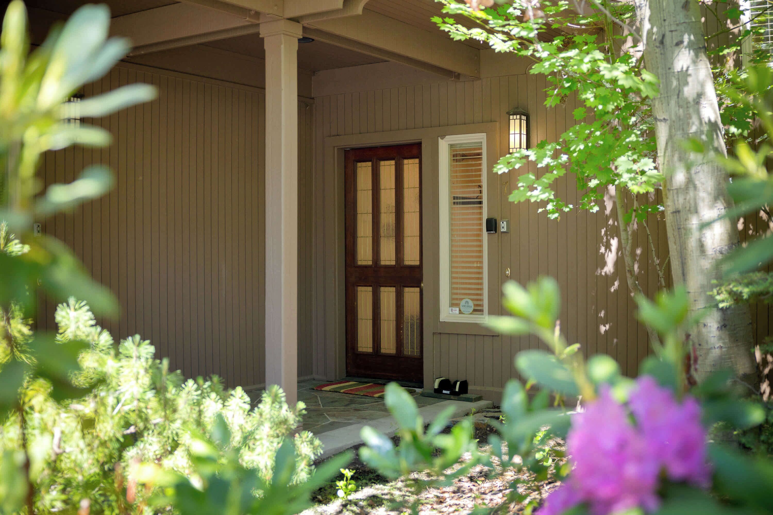 A house with a wooden door and white shutters, surrounded by greenery.