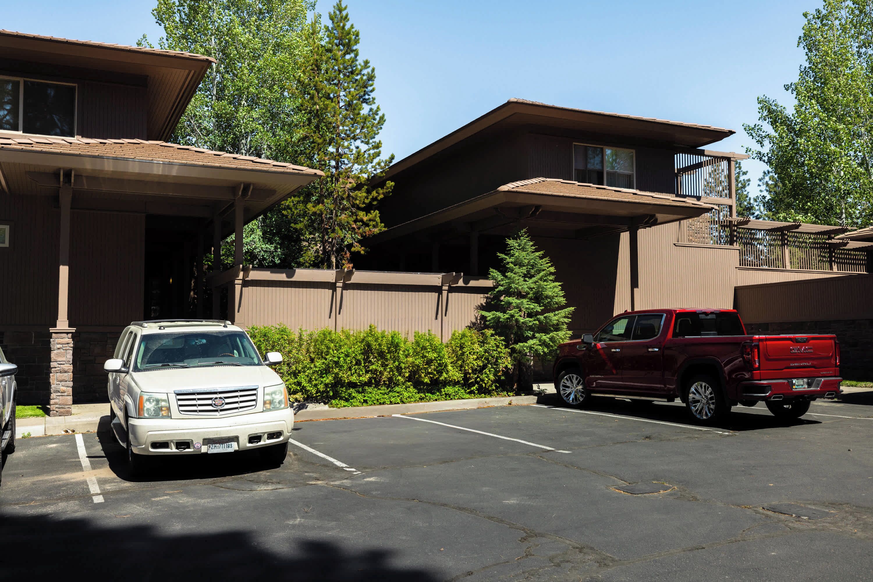 A parking lot with two vehicles, a white SUV and a red pickup truck, parked in front of a building with a flat roof and a balcony.