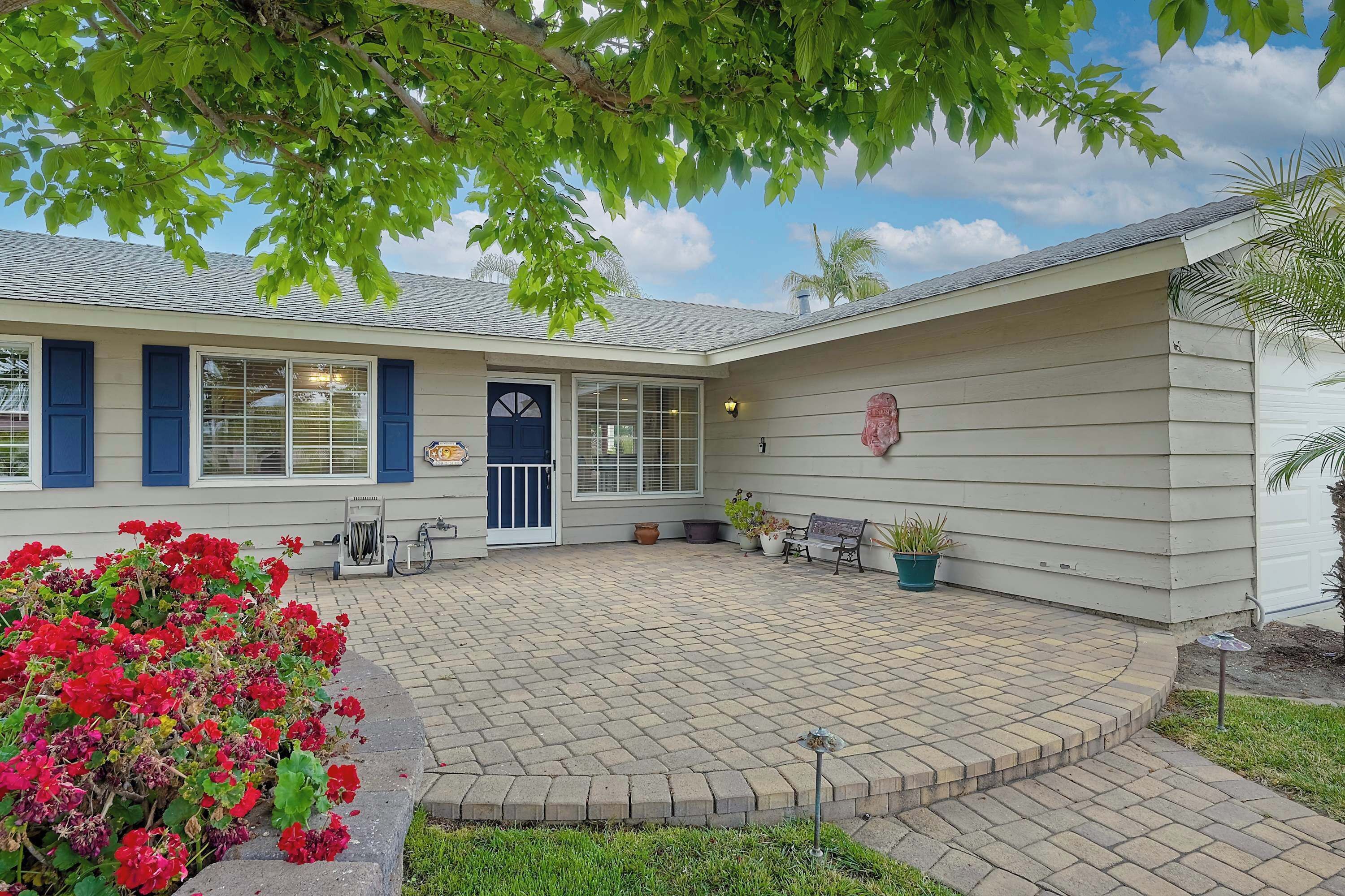 A house with a paved patio, a blue door, and a small garden with red flowers.