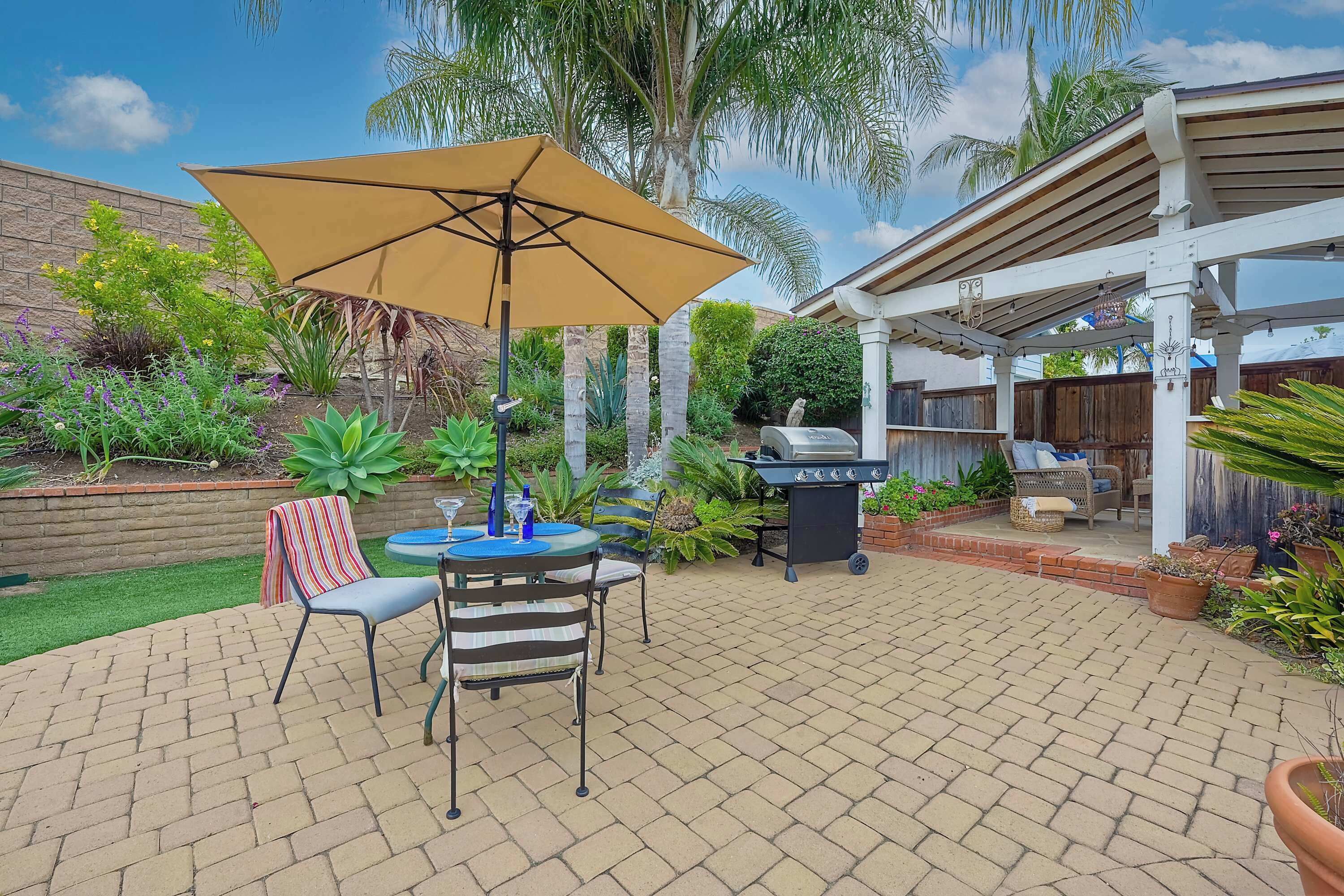 A patio with a table and chairs, a grill, and a covered area with a bench.