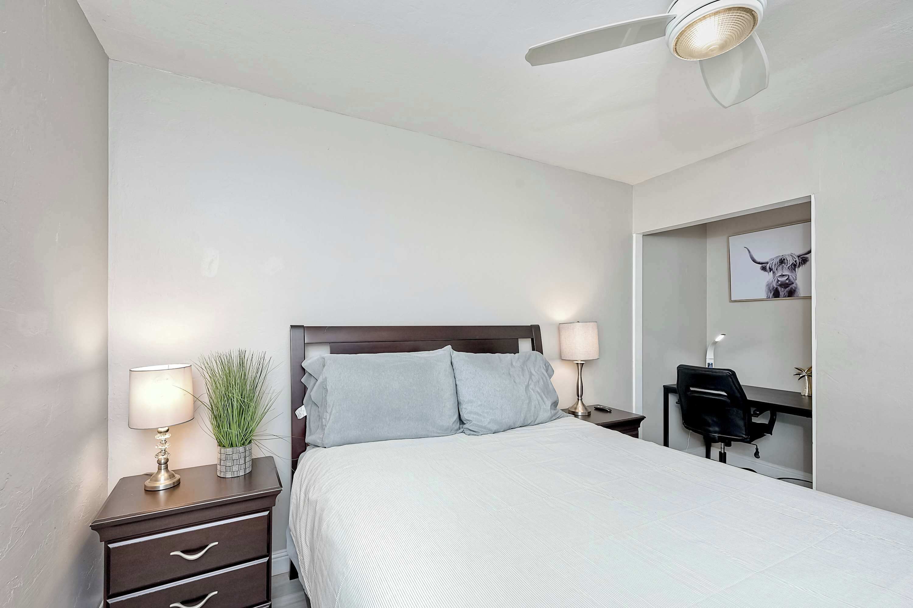 A neatly arranged bedroom with a bed, bedside tables, a desk, and a ceiling fan.