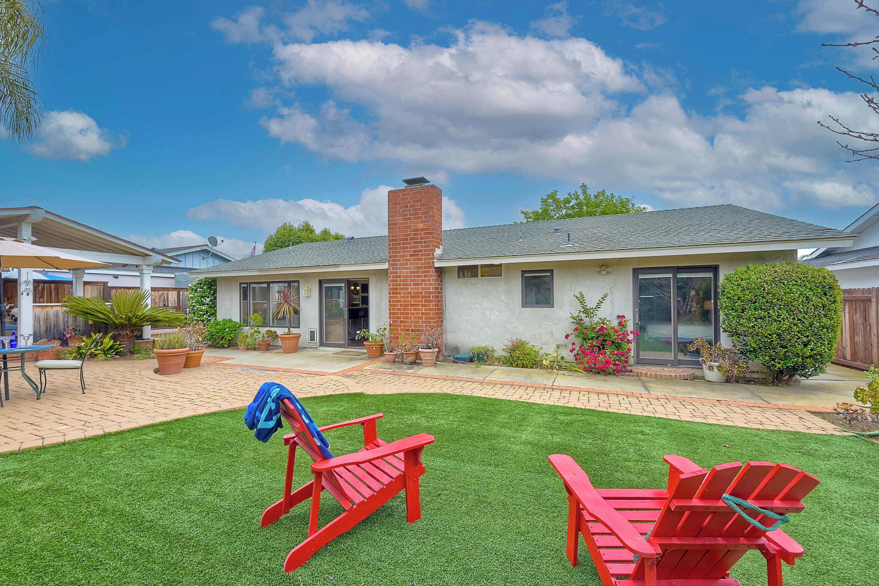 Un patio trasero residencial con césped, dos sillas Adirondack rojas y una chimenea de ladrillo.