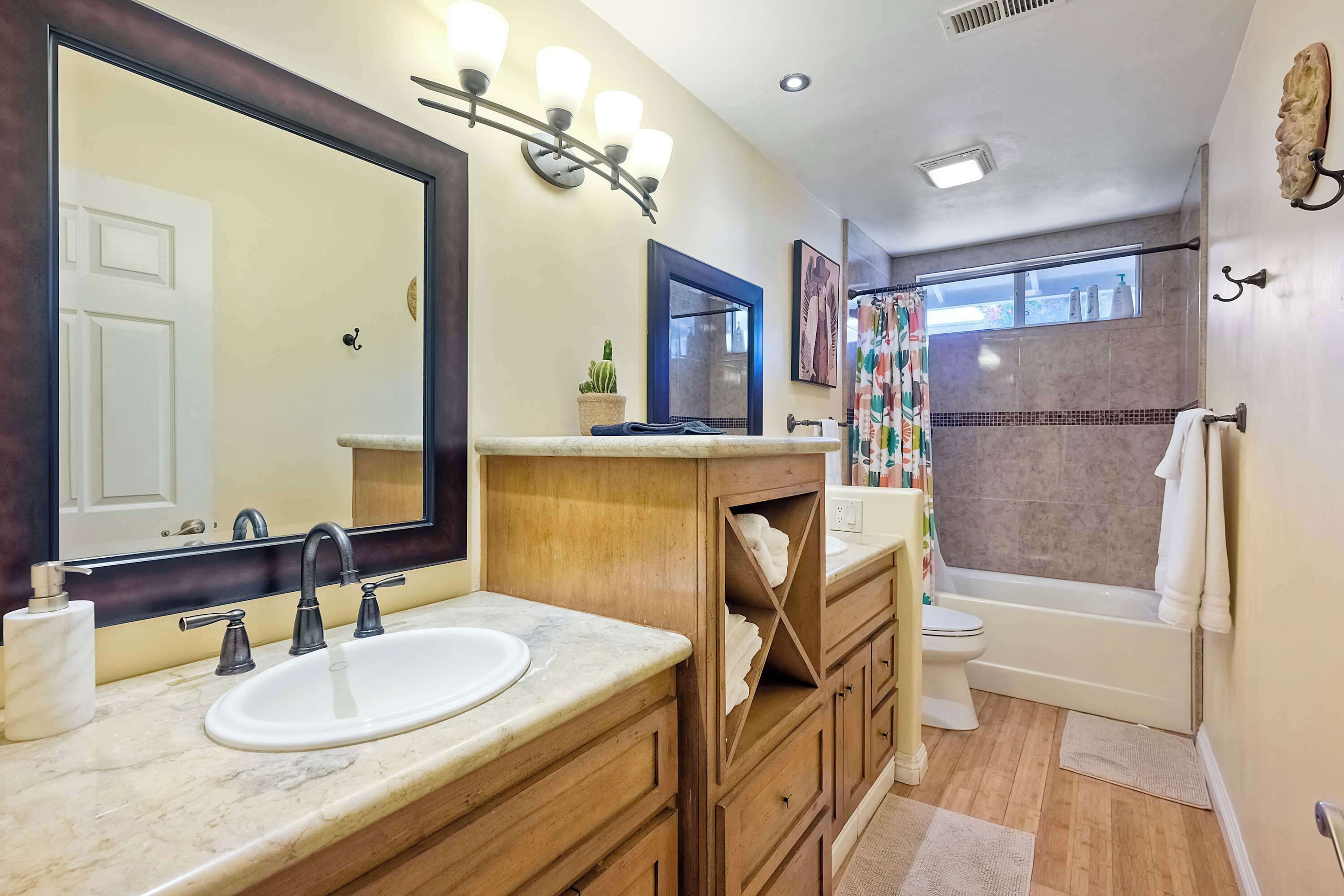 A bathroom with a sink, mirror, vanity, and a shower area.