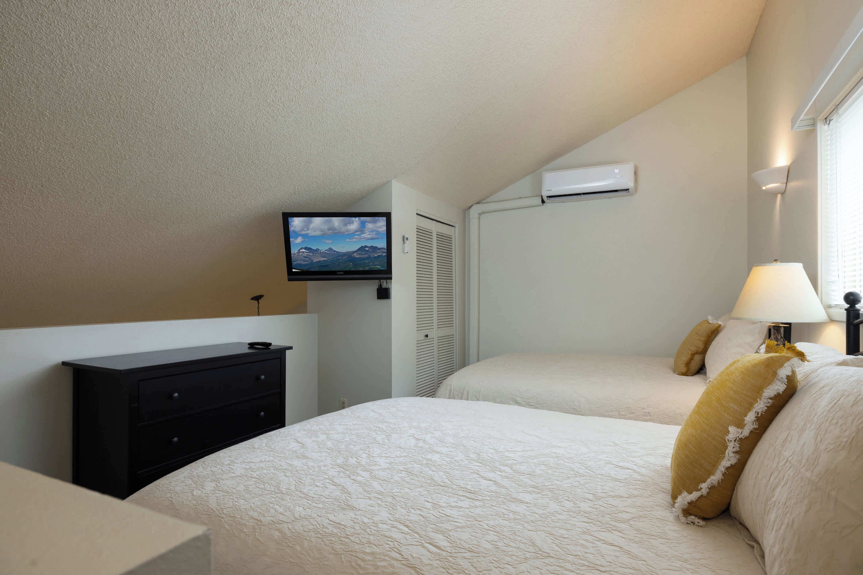Een slaapkamer met twee bedden, een aan de muur bevestigde televisie en een airconditioner.